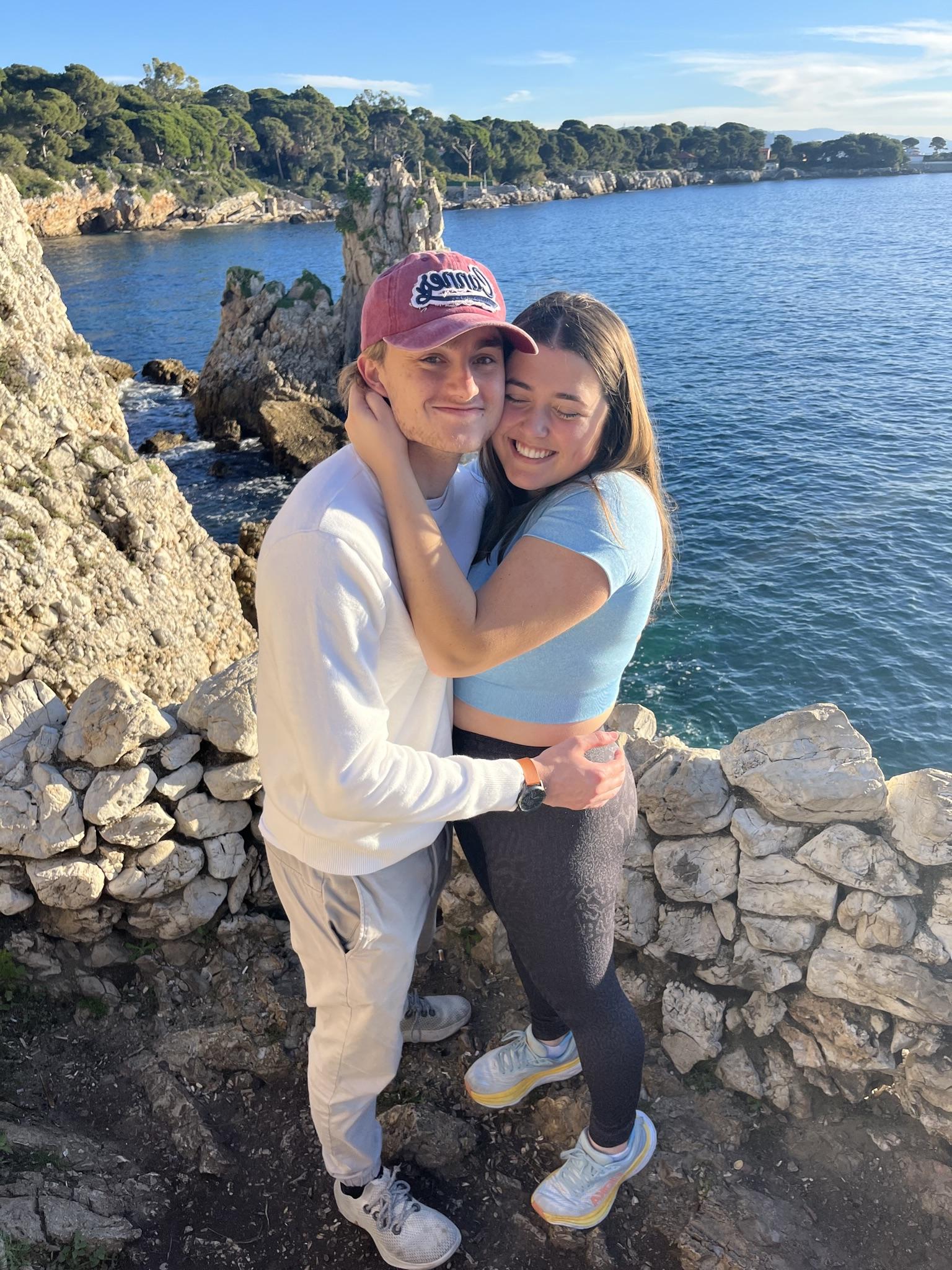 Couple hugging in front of water at Baie des Milliardaires at sunset.